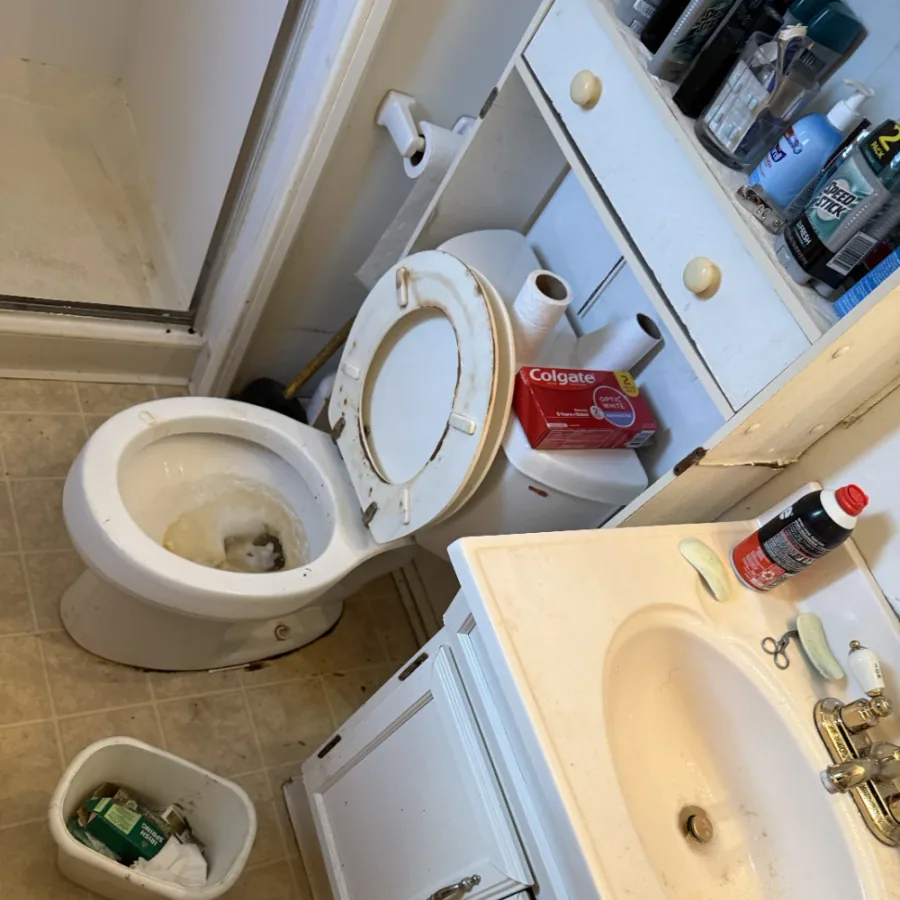 Bathroom vanity and toilet cluttered and stained before cleaning
